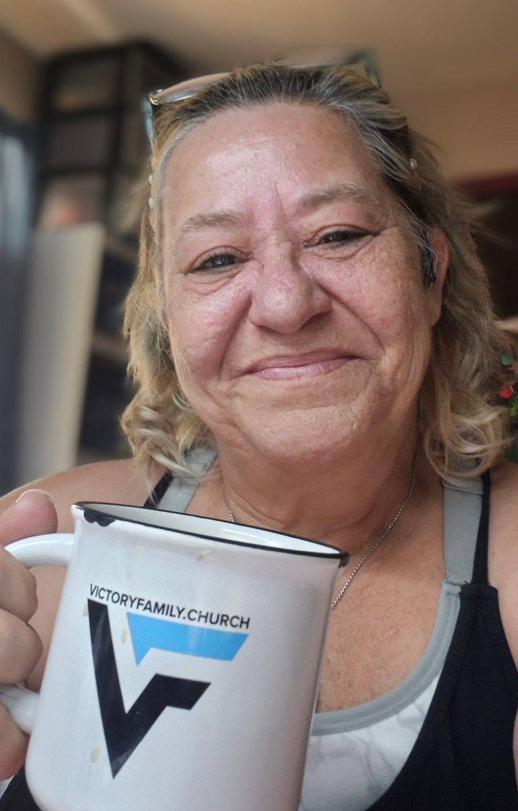 Virginia smiling while holding a coffee mug before sharing a personal story about neuropsychological testing, hope, and living with cognitive changes.